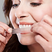 woman placing whitening stripe on smile